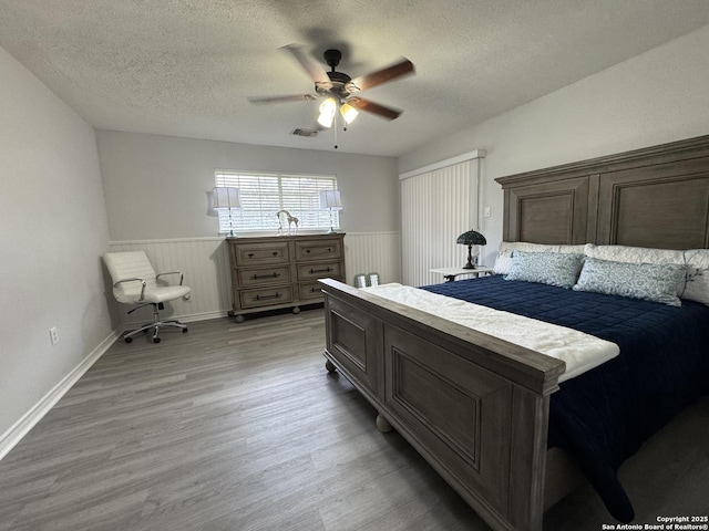 bedroom with light wood-type flooring, visible vents, a ceiling fan, a textured ceiling, and wainscoting