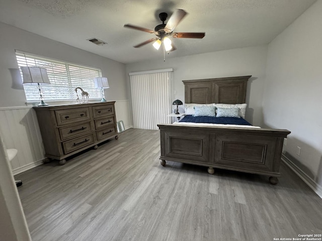 bedroom with visible vents, a textured ceiling, light wood-style flooring, and wainscoting