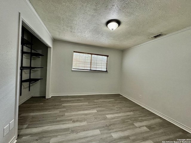 unfurnished room with visible vents, a textured ceiling, wood finished floors, and ornamental molding