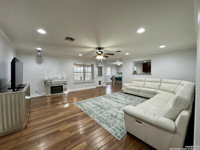 living room with baseboards, visible vents, a fireplace, ornamental molding, and wood-type flooring