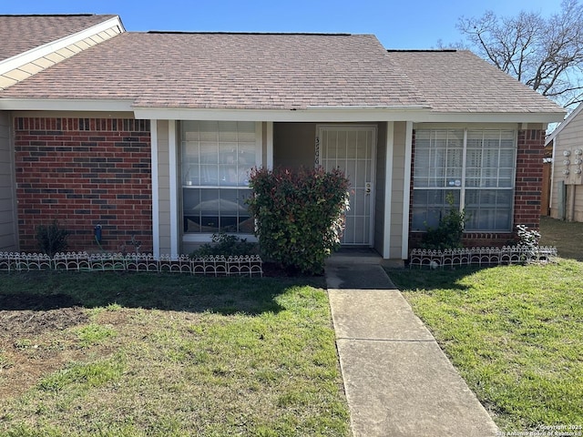 property entrance featuring brick siding, a lawn, and roof with shingles