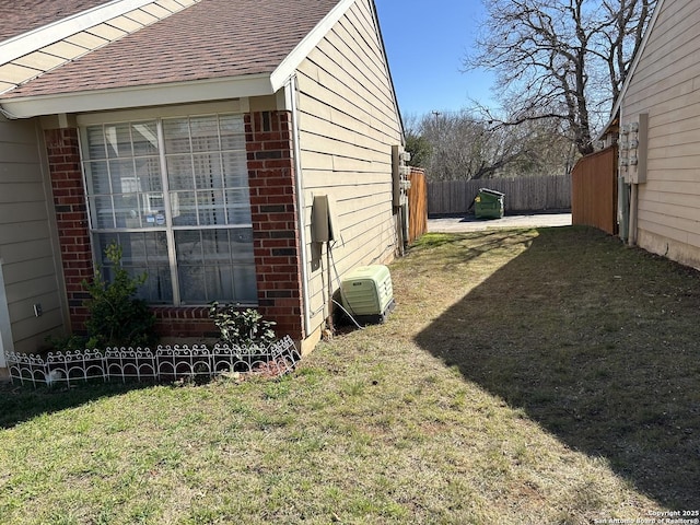 view of side of property with fence, brick siding, roof with shingles, and a lawn