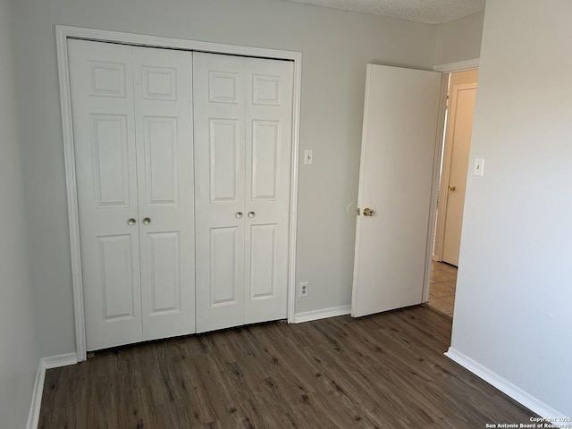 unfurnished bedroom featuring dark wood-style floors, baseboards, and a closet