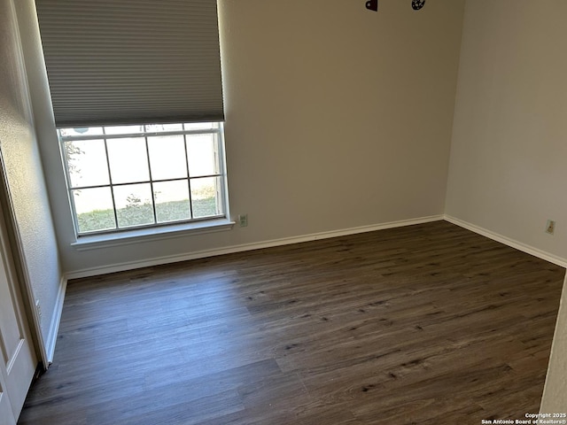 spare room with baseboards and dark wood-type flooring