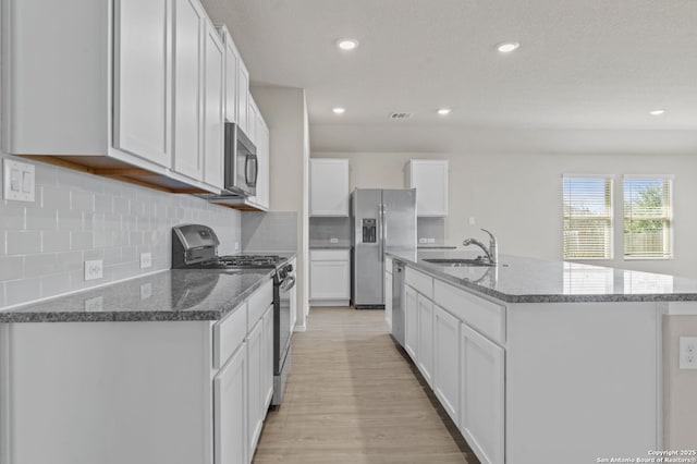 kitchen featuring visible vents, a sink, stainless steel appliances, white cabinetry, and a kitchen island with sink