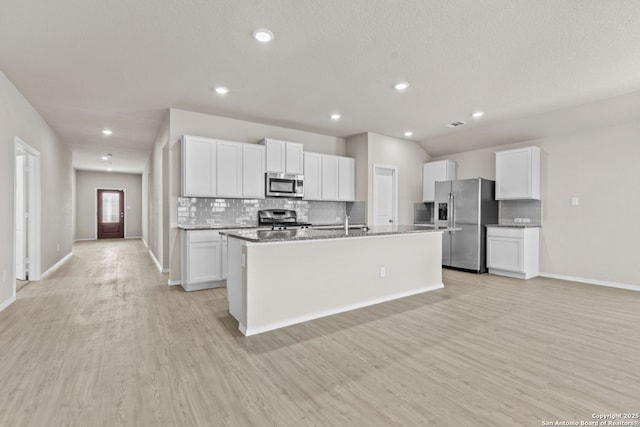 kitchen with light wood-style flooring, an island with sink, tasteful backsplash, white cabinetry, and stainless steel appliances