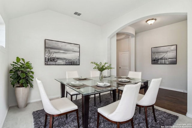 dining area with arched walkways, visible vents, baseboards, and vaulted ceiling