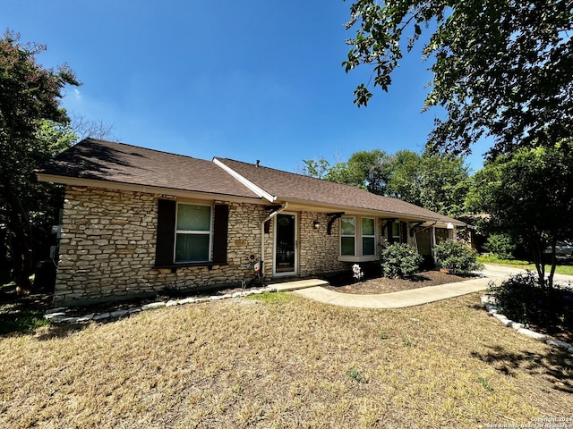 ranch-style house with stone siding, a front yard, and roof with shingles