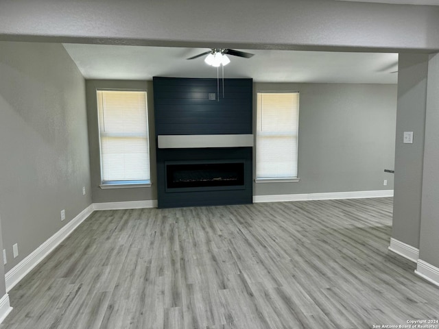 unfurnished living room featuring a wealth of natural light, baseboards, a large fireplace, and wood finished floors