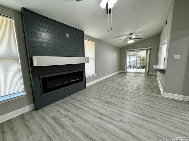 unfurnished living room featuring wood finished floors, a ceiling fan, baseboards, vaulted ceiling, and a large fireplace