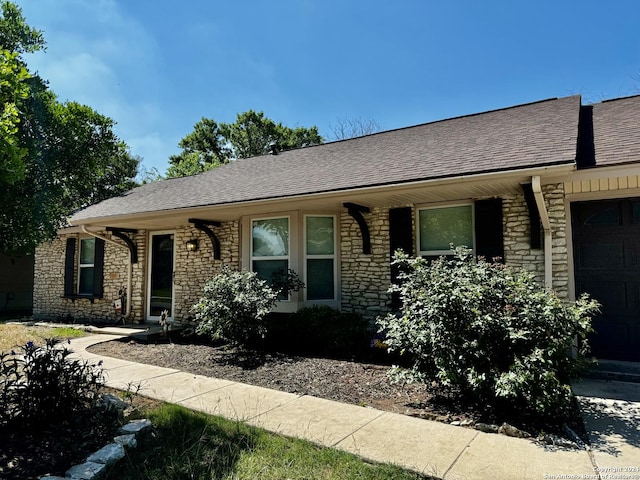 single story home featuring stone siding, roof with shingles, and an attached garage