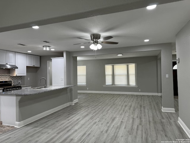 kitchen featuring light wood-style flooring, stainless steel range, under cabinet range hood, light stone counters, and backsplash