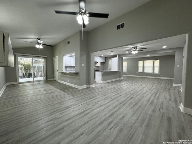 unfurnished living room with lofted ceiling, wood finished floors, visible vents, and baseboards