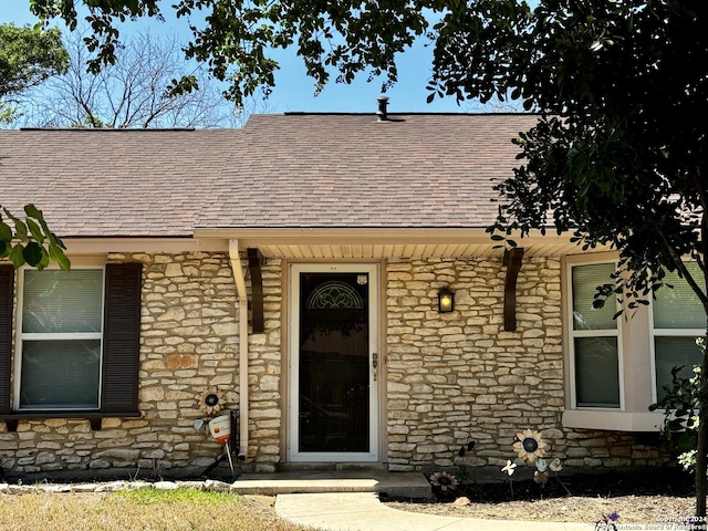 entrance to property with stone siding and a shingled roof