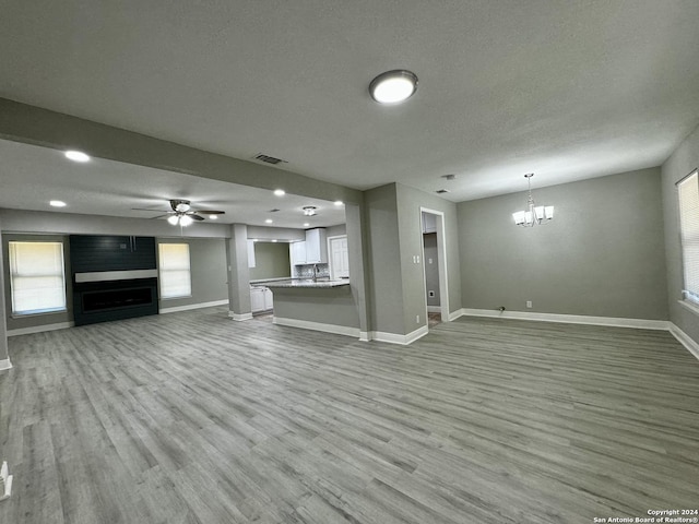 unfurnished living room with visible vents, ceiling fan with notable chandelier, a large fireplace, and wood finished floors