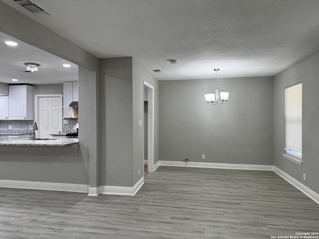 unfurnished dining area featuring visible vents, baseboards, an inviting chandelier, and light wood-style flooring