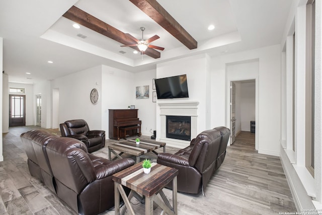 living area with light wood-style flooring, a glass covered fireplace, a ceiling fan, visible vents, and a raised ceiling