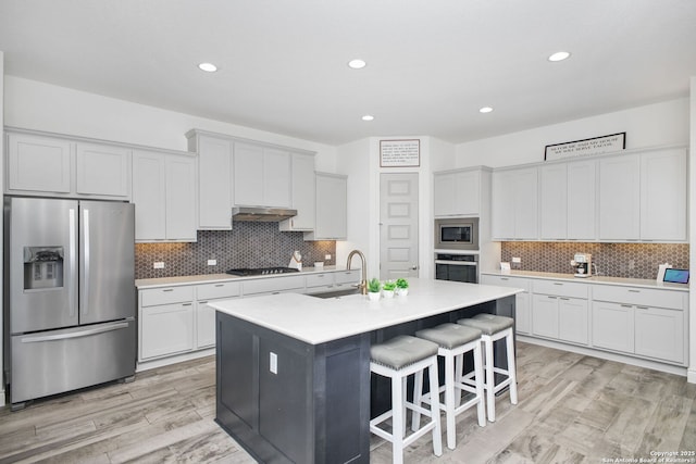 kitchen with appliances with stainless steel finishes, a kitchen breakfast bar, under cabinet range hood, decorative backsplash, and a sink