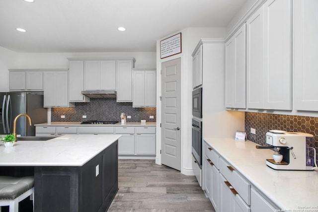 kitchen with tasteful backsplash, light wood-type flooring, under cabinet range hood, stainless steel appliances, and a sink