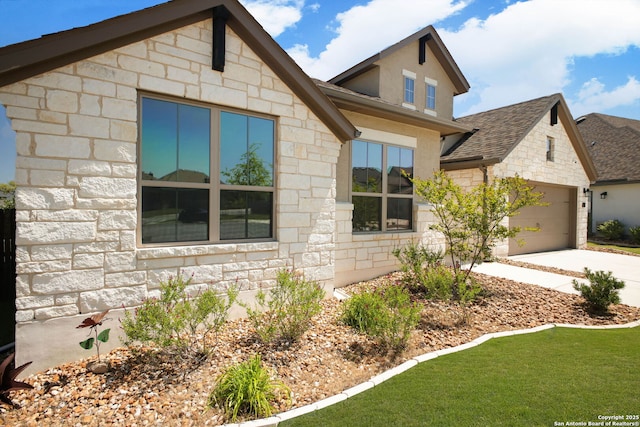 view of front facade featuring concrete driveway, an attached garage, stone siding, and a shingled roof