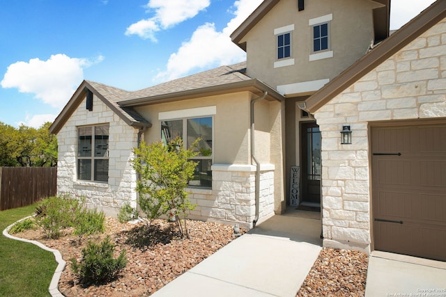 entrance to property featuring stucco siding, stone siding, fence, and a shingled roof