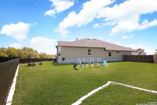 rear view of house with a yard, a fenced backyard, a playground, and stucco siding