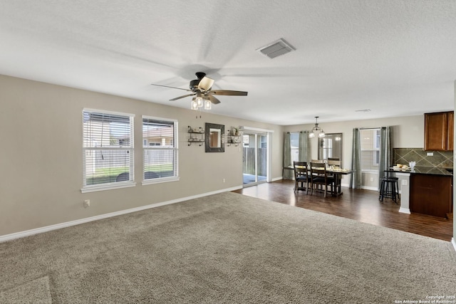 unfurnished living room with visible vents, a healthy amount of sunlight, baseboards, and dark colored carpet