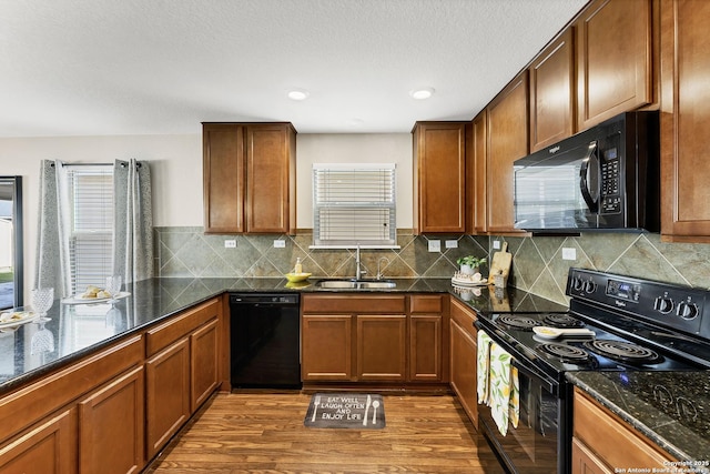 kitchen with black appliances, dark stone counters, dark wood-type flooring, and a sink