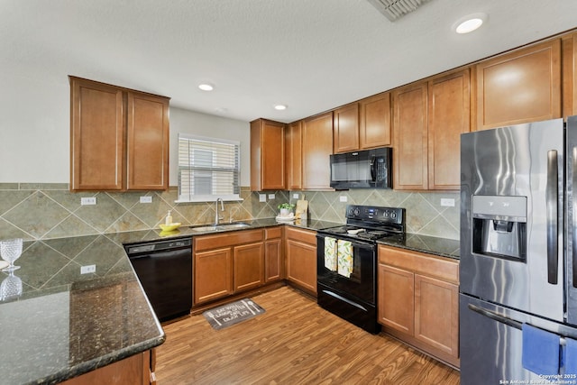 kitchen with tasteful backsplash, visible vents, light wood-type flooring, black appliances, and a sink