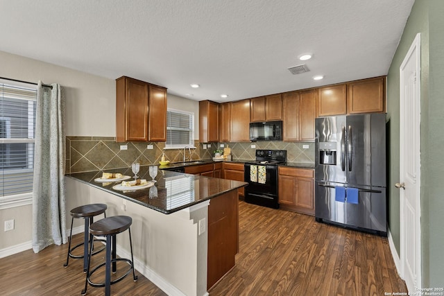 kitchen featuring visible vents, dark wood finished floors, a peninsula, a sink, and black appliances