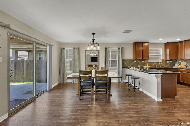 dining space with dark wood finished floors, baseboards, visible vents, and a chandelier