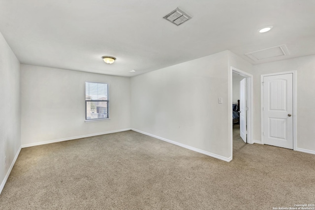 carpeted spare room with attic access, baseboards, and visible vents