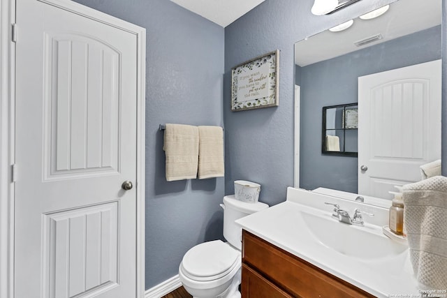 bathroom with vanity, toilet, a textured wall, and visible vents