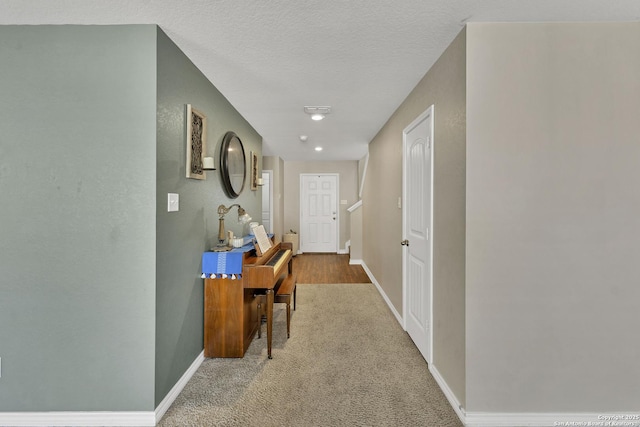 hallway featuring baseboards, a textured ceiling, and carpet floors