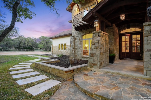 view of exterior entry with french doors, stone siding, and a balcony