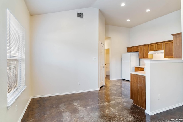 kitchen featuring visible vents, baseboards, under cabinet range hood, freestanding refrigerator, and brown cabinetry