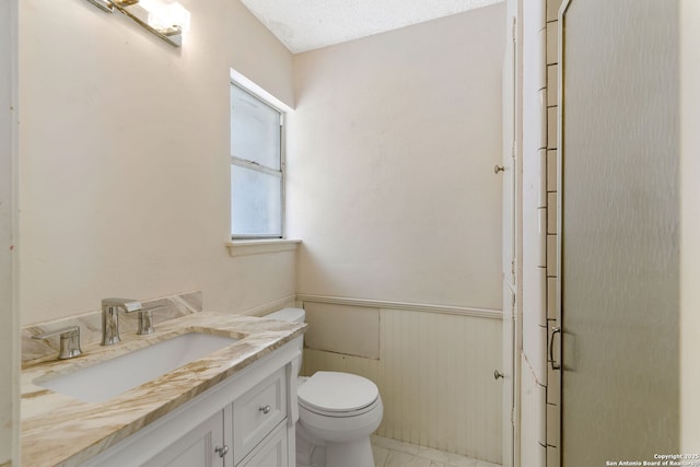 bathroom with a wainscoted wall, toilet, and vanity