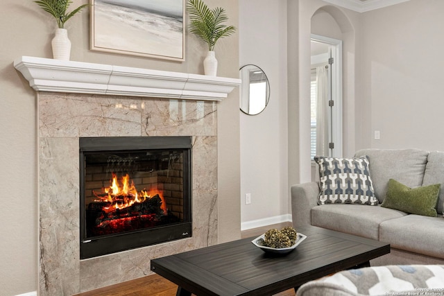 living room featuring wood finished floors, a fireplace, arched walkways, and baseboards