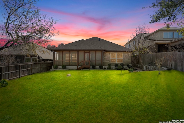 rear view of property featuring a yard, a fenced backyard, and a sunroom