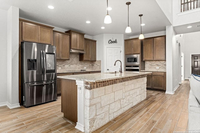 kitchen featuring light stone countertops, wood tiled floor, a sink, under cabinet range hood, and appliances with stainless steel finishes