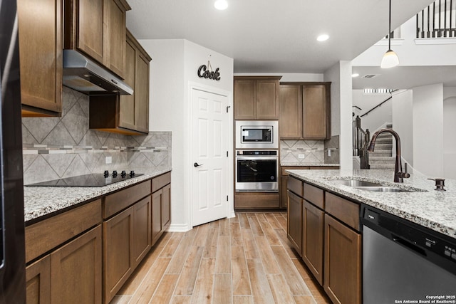 kitchen featuring light wood finished floors, light stone countertops, under cabinet range hood, appliances with stainless steel finishes, and a sink