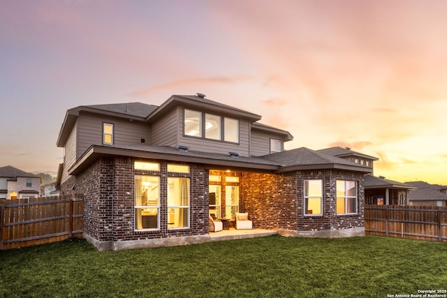 back of property featuring brick siding, a patio area, a yard, and fence