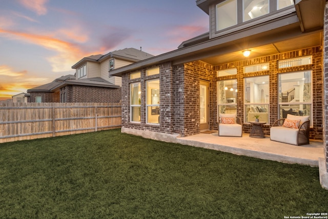 rear view of property featuring a patio area, fence, brick siding, and a lawn