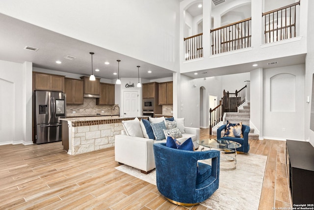 living room with arched walkways, visible vents, light wood-type flooring, and stairs