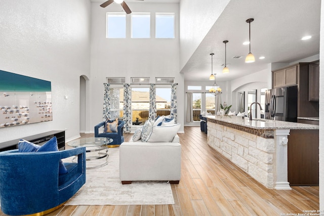 living area featuring recessed lighting, light wood-style flooring, ceiling fan with notable chandelier, a high ceiling, and arched walkways