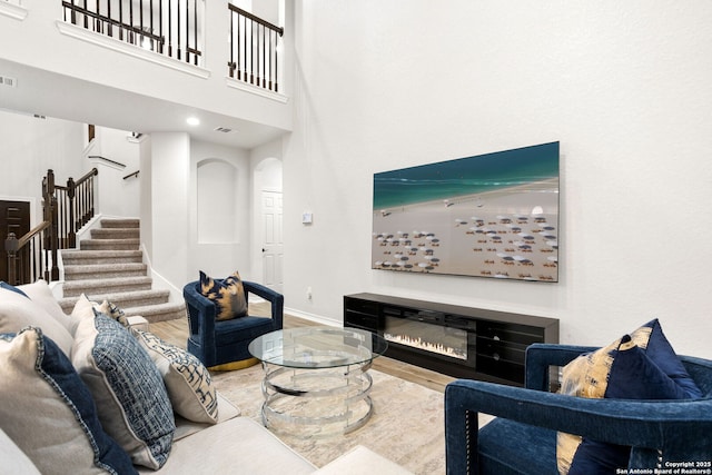 living room featuring visible vents, baseboards, stairs, wood finished floors, and a glass covered fireplace