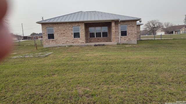 rear view of house featuring fence, a standing seam roof, a yard, brick siding, and metal roof