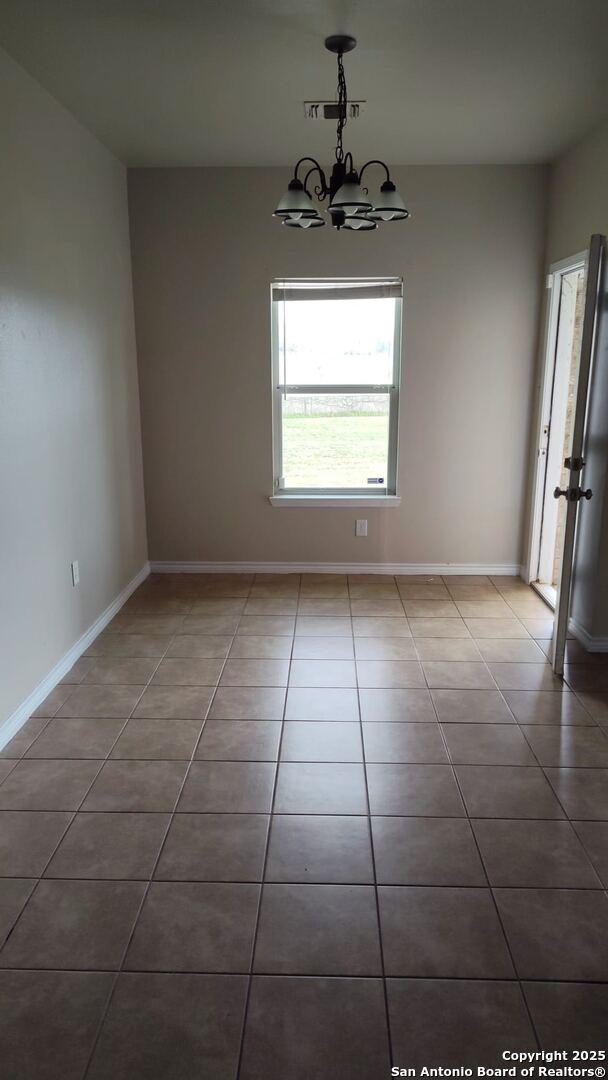 unfurnished room featuring tile patterned floors, baseboards, and a chandelier