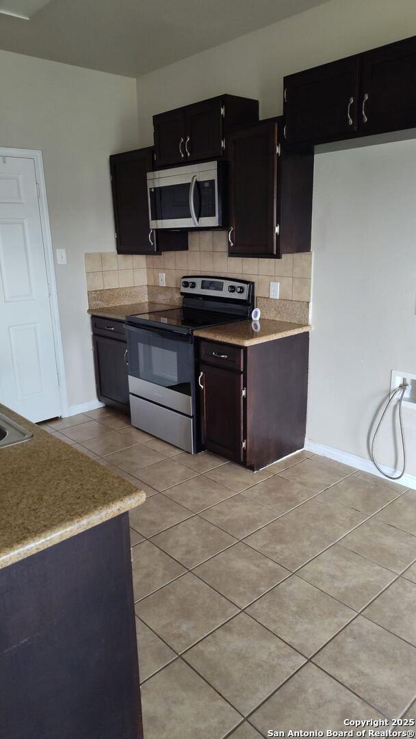 kitchen with light tile patterned floors, tasteful backsplash, appliances with stainless steel finishes, and dark cabinets