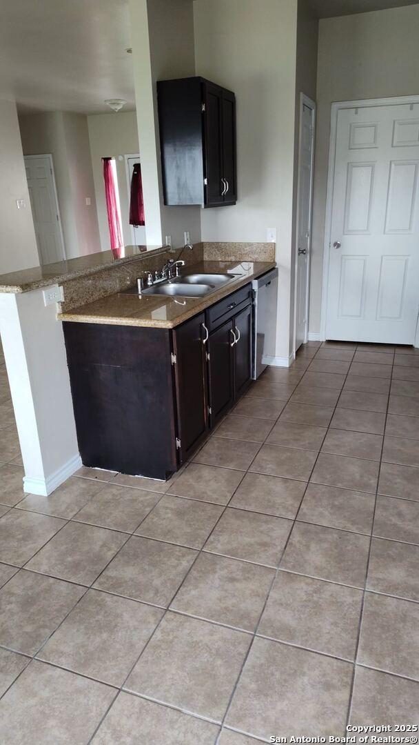 kitchen featuring light tile patterned floors, baseboards, stone countertops, a sink, and stainless steel dishwasher